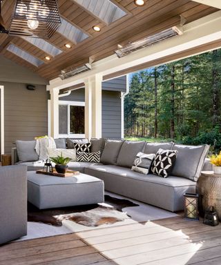 Patio porch with downlights and pendant light, outdoor living space, gray sectional and footstool, rugs, couch pillows in geometric black and white assortment of patterns