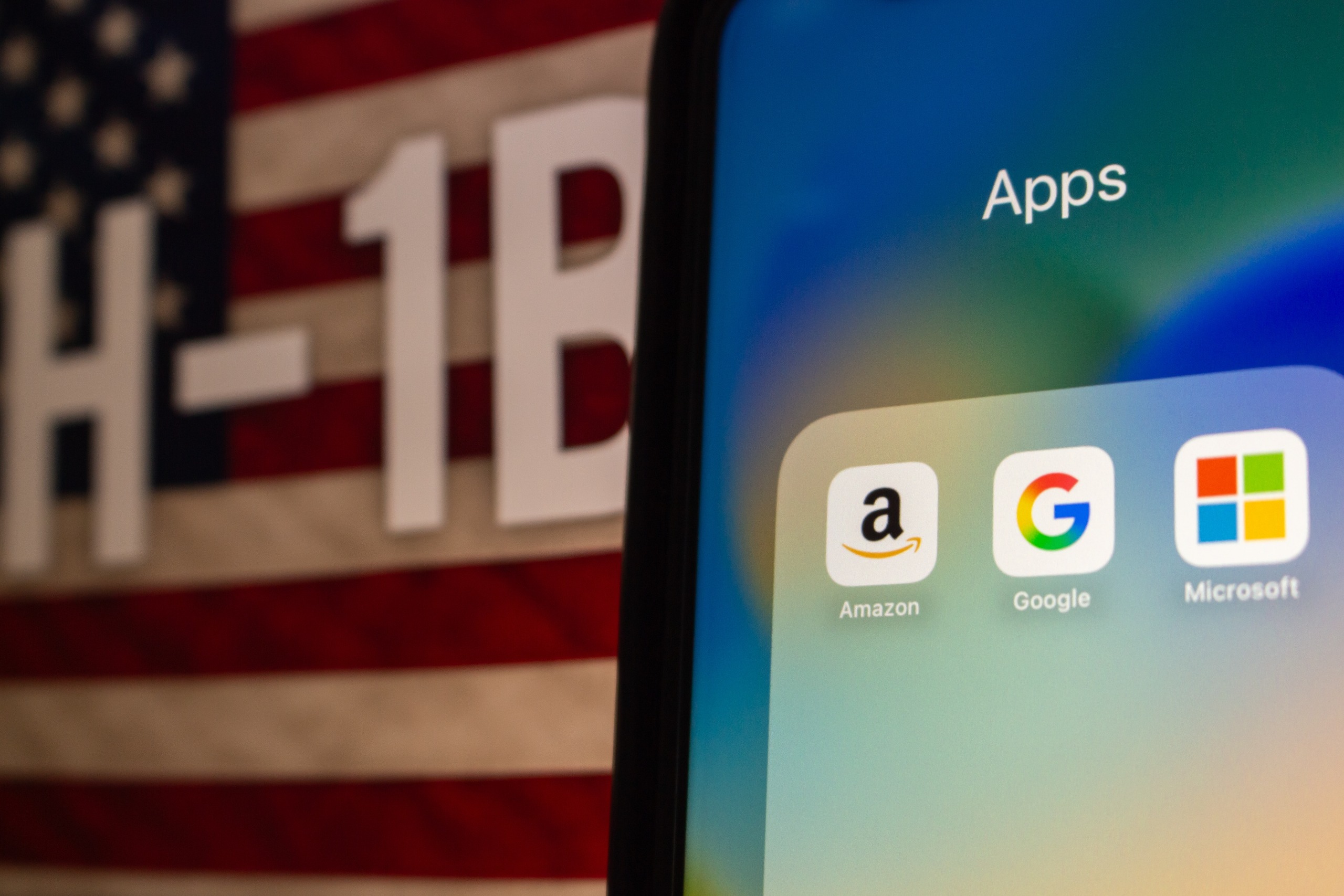 Smartphone screen showing Amazon, Google, and Microsoft icons in front of an American flag and H-1B VASA reference, symbolizing tech jobs, VISA and job offer in US.