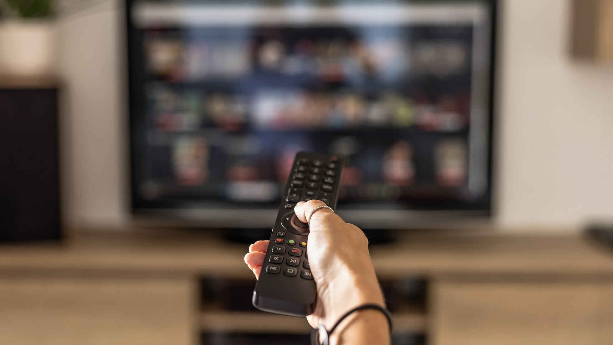 A hand holding a remote pointed at television with a streaming menu on the screen