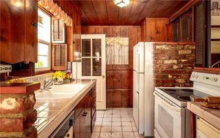 A dated kitchen with wood panelled walls, white countertops, and wooden window shutters
