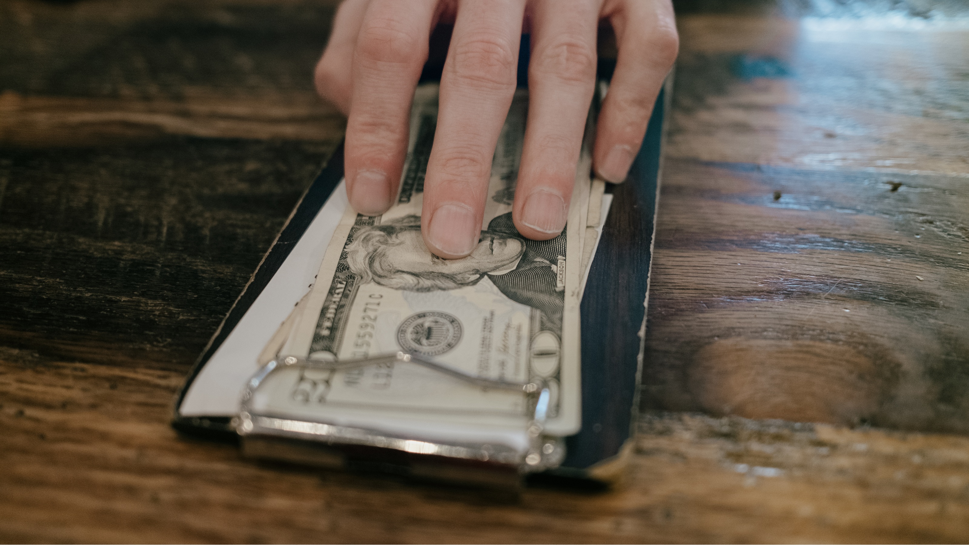 Cash in a money tray at a restaurant, a man's fingers seeming to push it across the table.