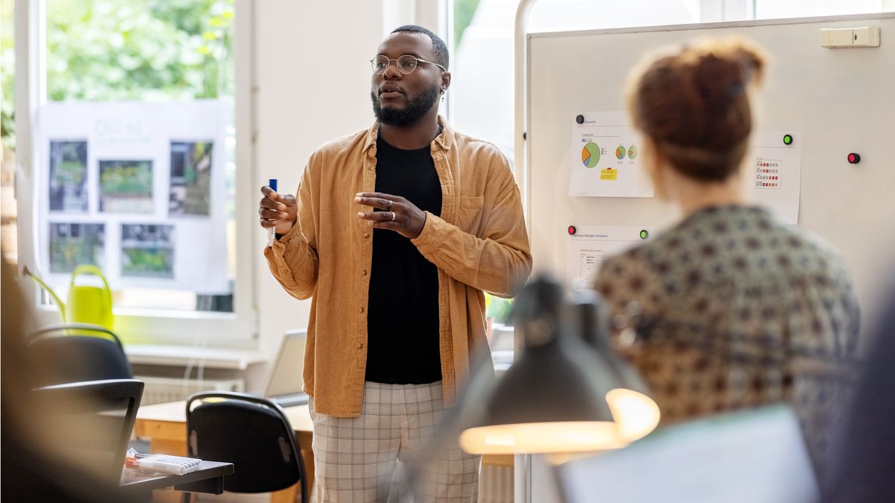 A man stands in front of a group of co-workers to give a sales presentation.