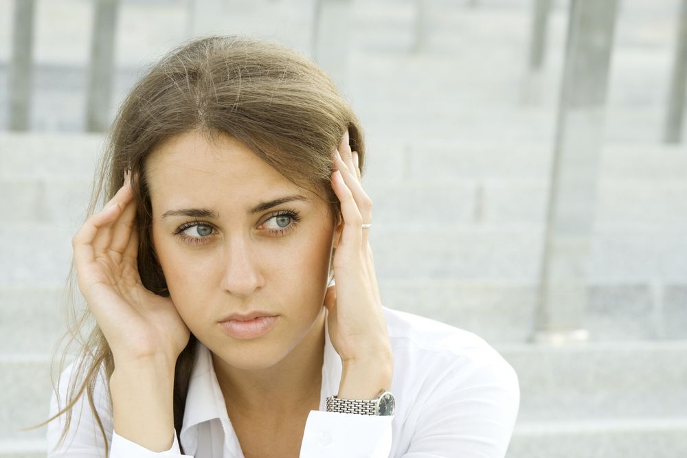 A dizzy young woman sits down and holds her head.