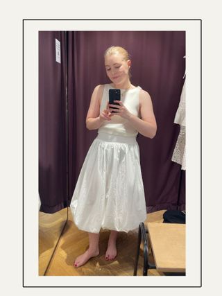 Woman in dressing room wears white top and white bubble hem skirt