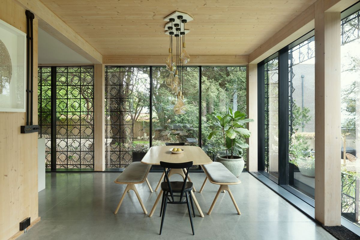 A dining room with glass walls and a dinner table with a statement pendant light above it