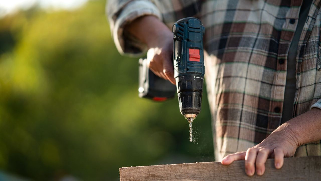 A female carpenter using a power drill on a piece of wood outside