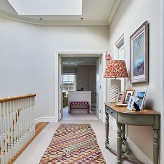 a long carpeted landing area with a colourful patterned floor runner, a green grey console table against the wall and open double doors leading to another room