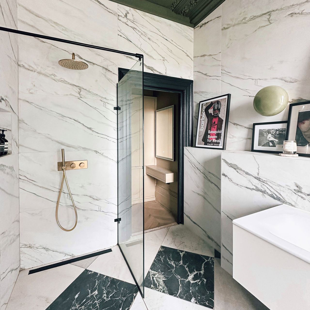 Bathroom with marble walls and floor, ledge with framed artworks and glass lined walk-in shower