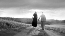 A couple walks hand-in-hand down a country road.