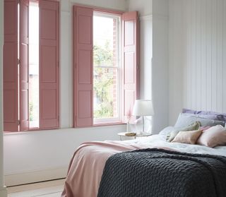 bedroom with pastel pink shutters and pastel bedding, ice cream shades, grey blanket, white walls, white painted floorboards