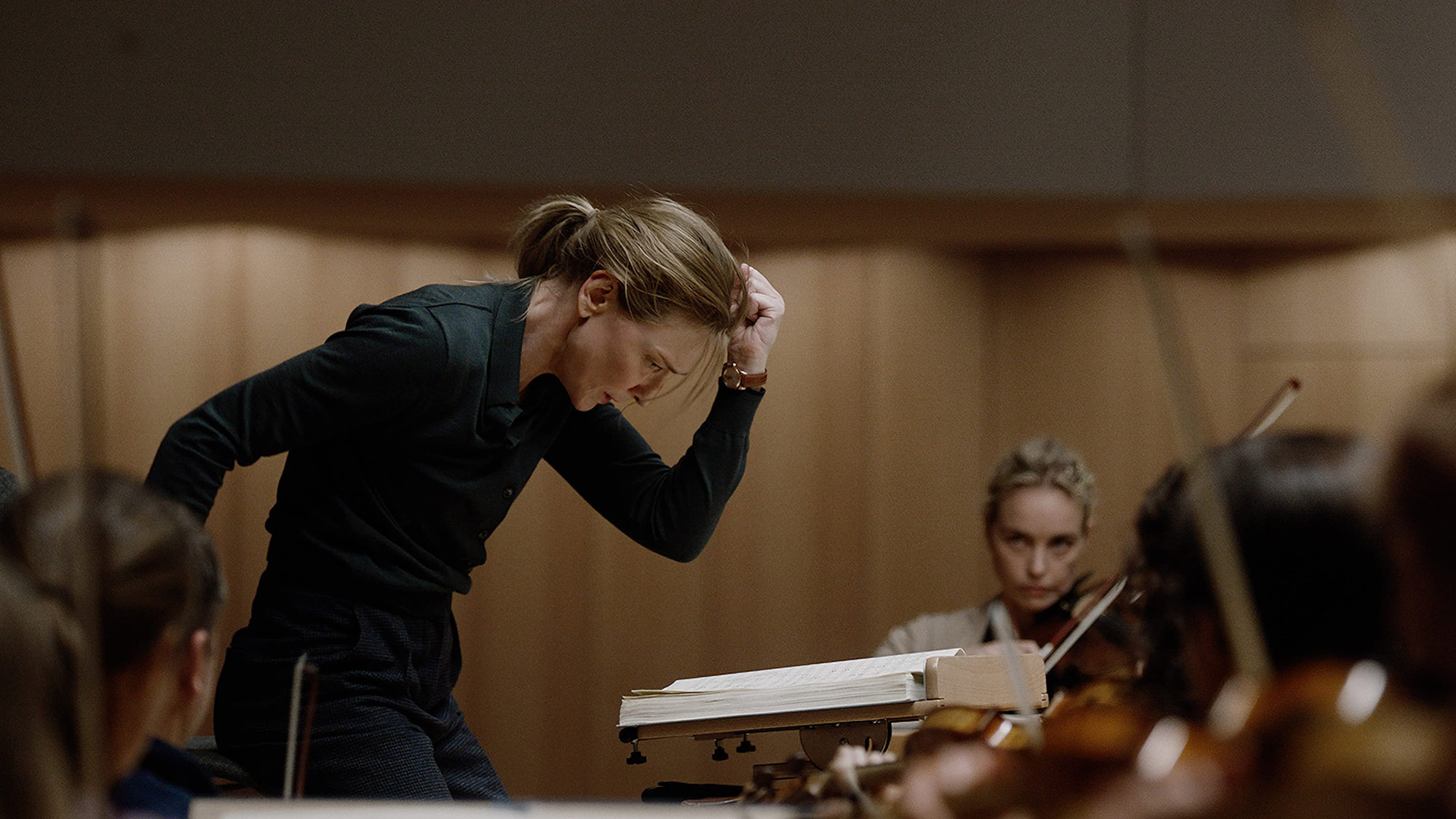 A still from the movie Tar in which the main character Tar, played by Cate Blanchett, is conducting an orchestra.