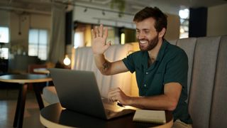 A man using a laptop while waving at a person on a video call