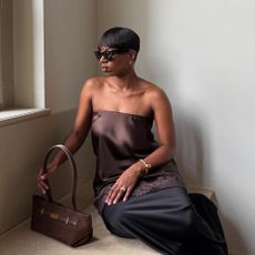 Influencer @thevisuelofgrace wears a satin top with a black satin skirt and brown suede handbag.