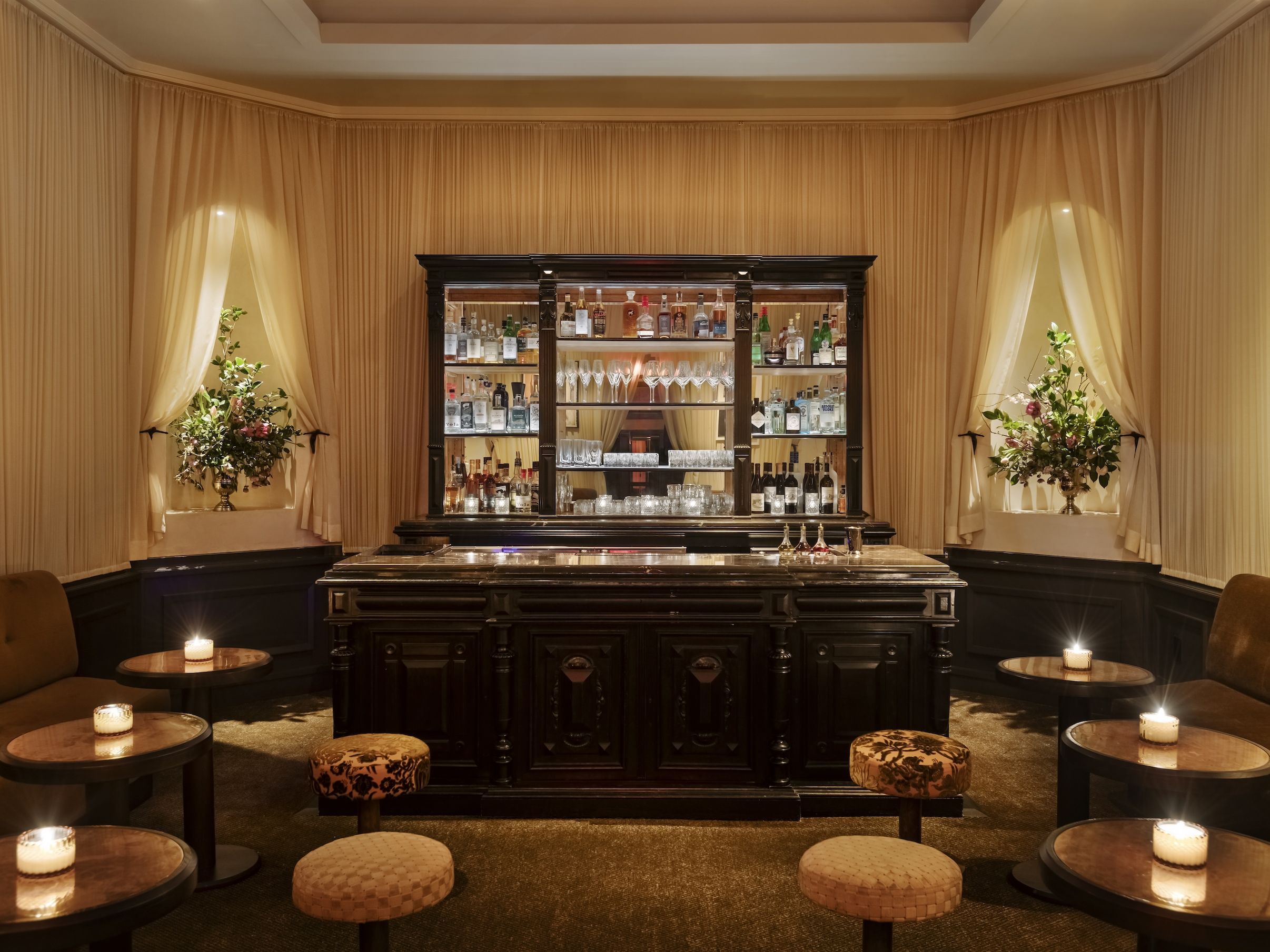 A sumptuously decorated bar features warm Art Deco lighting, refined cabinetry, and curtain-paneled walls.