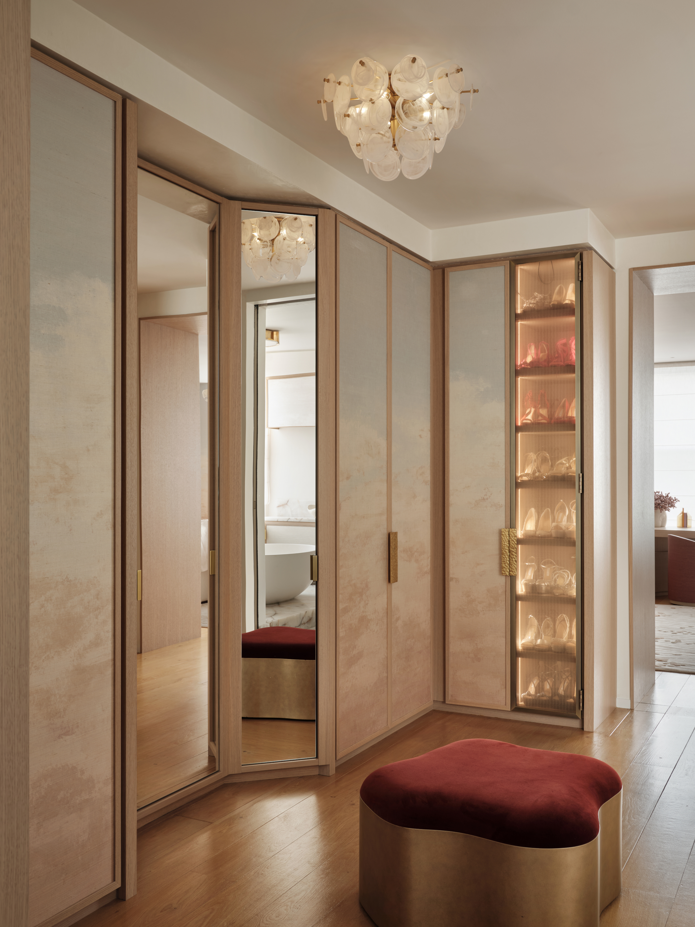 Dressing area with built-in wardrobes with wallpapered and mirrored doors, plus central stool in brass and burgundy velvet