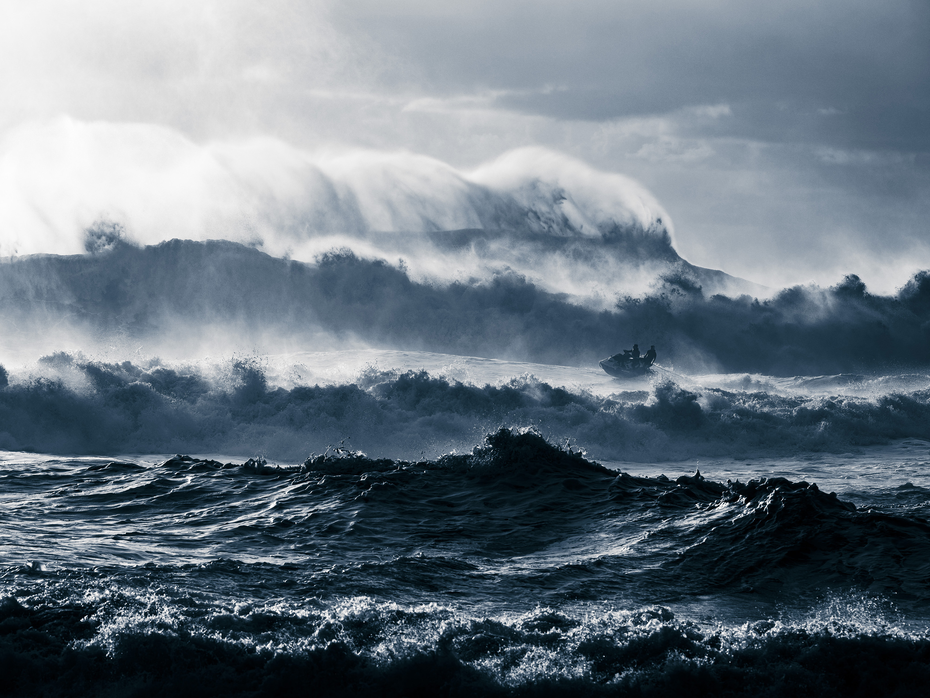 Two people surf among massive ocean waves