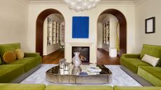 Living room with cream walls, wall-to-wall green velvet corner sofa, chrome coffee table and cobalt blue artwork