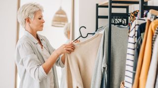 Woman sorting through her wardrobe, holding an item on a rack