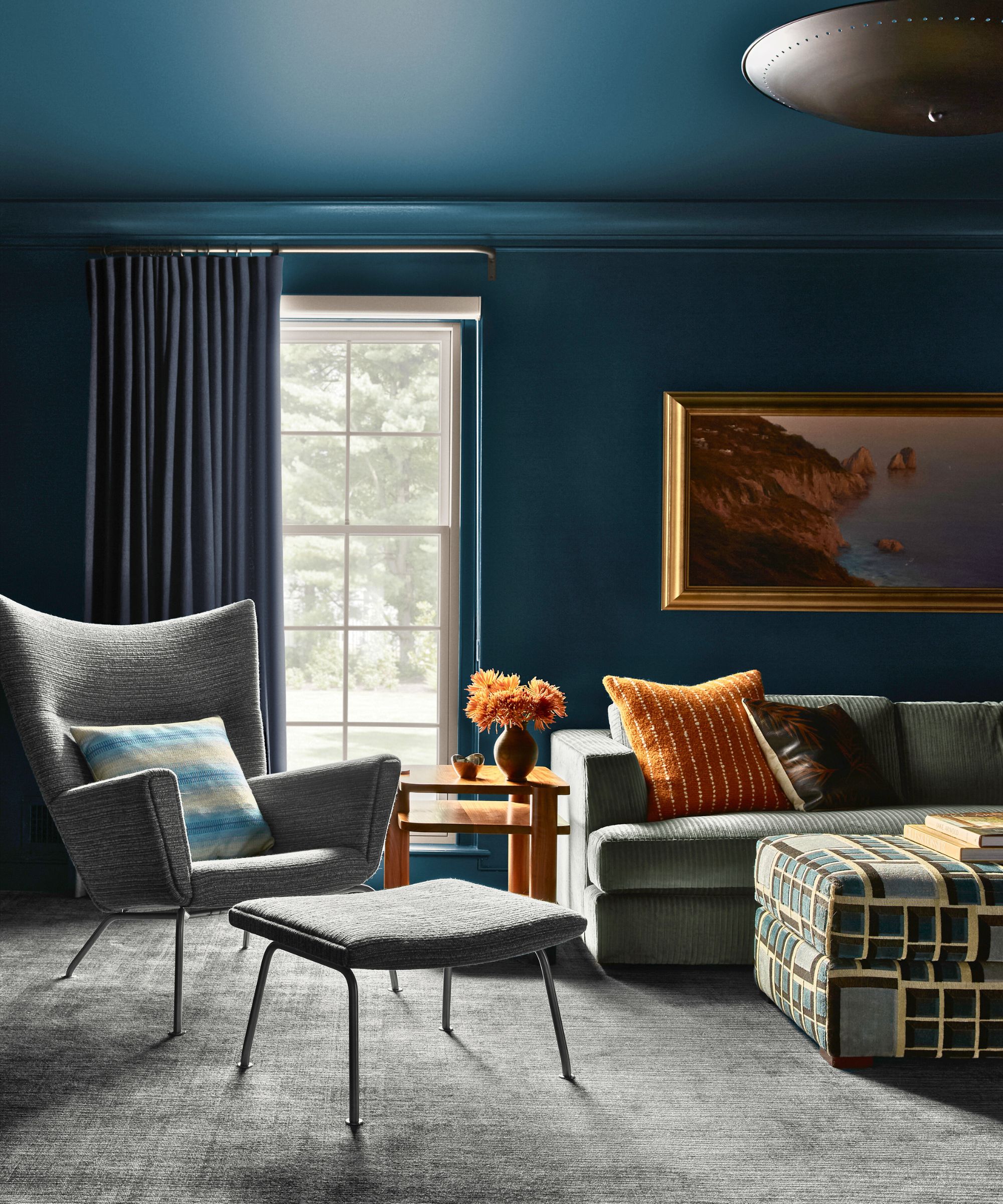 living room color drenched in dark blue with gray sofa and armchair, orange throw pillows and large painting in a gold frame