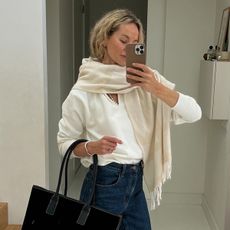  @anoukyve wearing a white sweater, white scarf, jeans, boots, and a black bag.