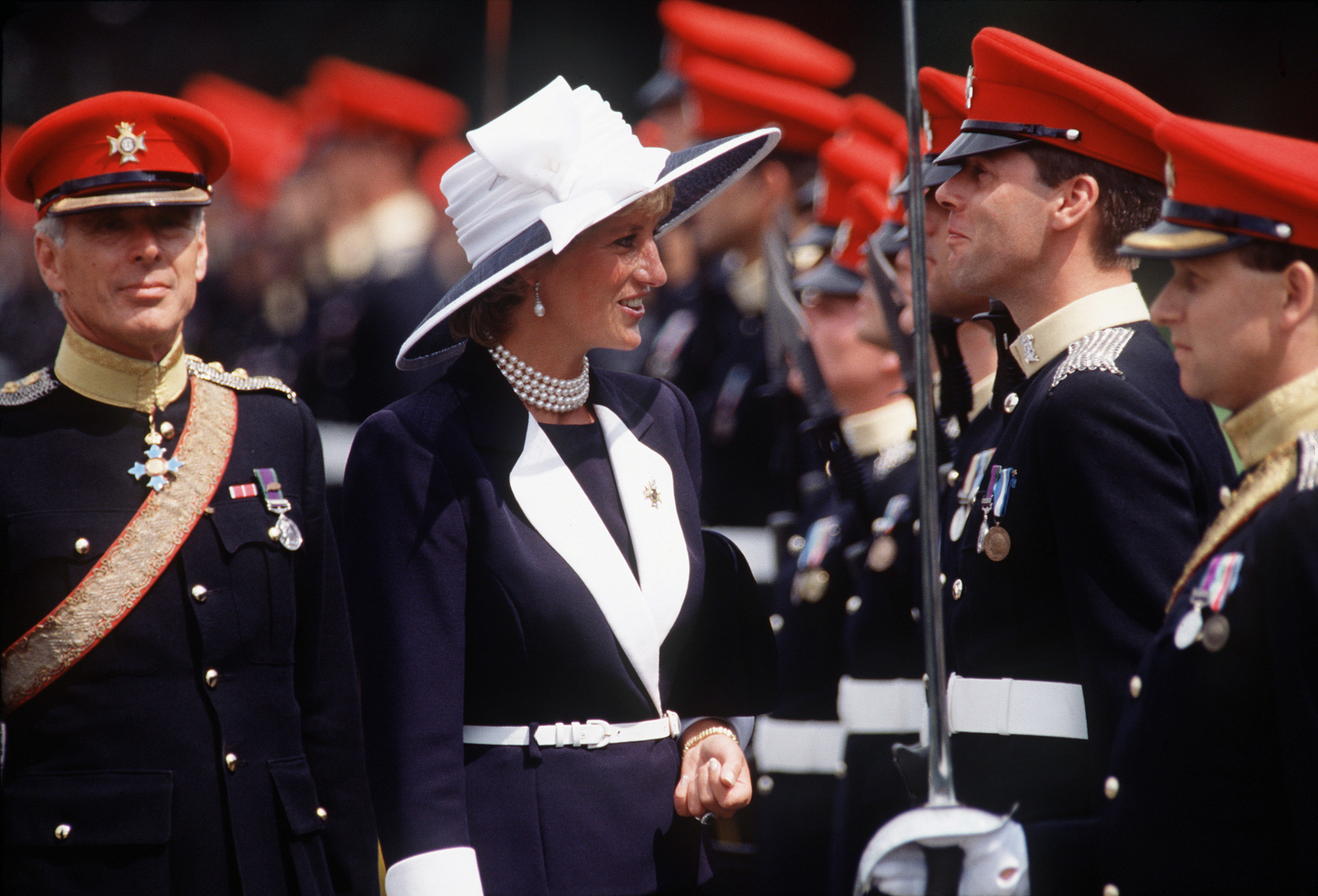 Princess Diana in a navy and white suit inspecting military soldiers