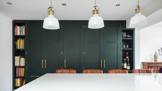 Forest green kitchen with brass handles and white ceramic pendants above a white marble kitchen island