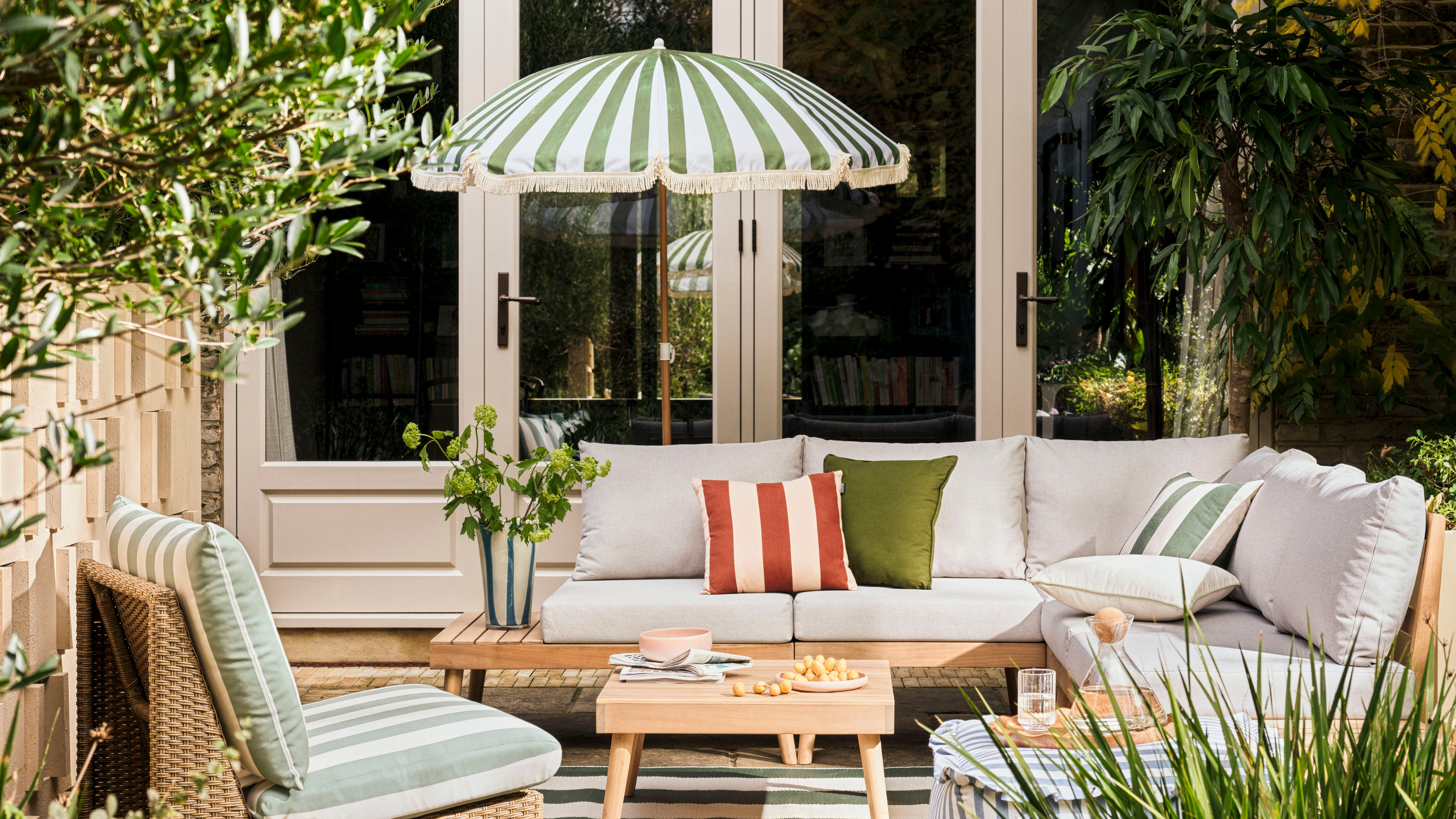 Habitat green striped Sunbeam parasol on a patio. There is a green striped garden accent chair, grey sofa set and wood coffee table.