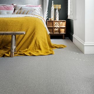 Grey ribbed carpet with double bed and mustard yellow blanket, bedside table