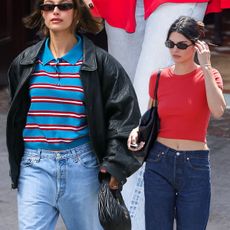 Hailey Bieber in Levi jeans, a striped polo sweater, and a leather bomber jacket. Kendall Jenner is in a red, fitted crewneck and dark rinse Levi's jeans, paired with black flip-flops and sunglasses. Dakota Johnson is in an oversized red button-down and pale Levi jeans. 