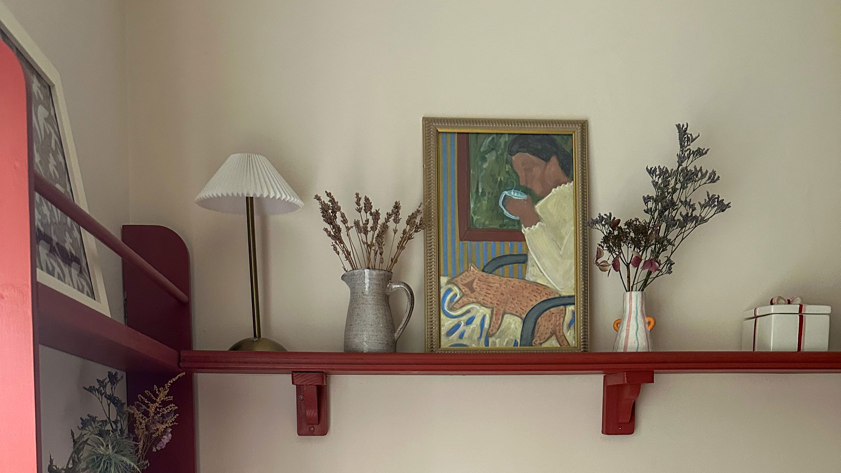 Red painted open shelving holding artwork, flowers in vases and a lamp