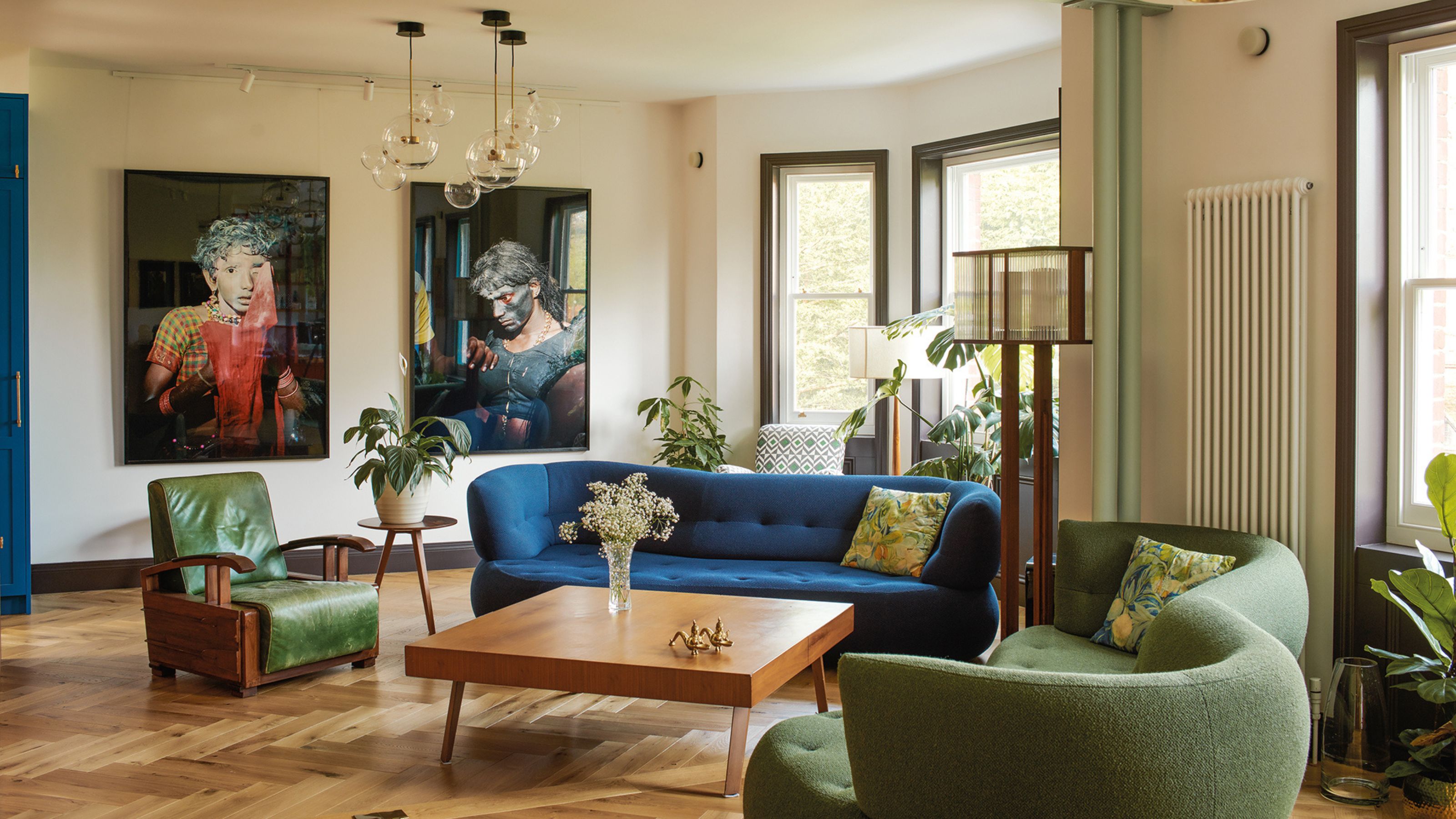 modern living room with blue sofa and green sofa and armchair with timber floors, large artworks, square timber coffee table, radiator on the wall, floor lamp, and pendant lights