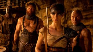 Furiosa stands with a gun slung over her shoulder with three other people behind her blurred out