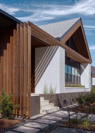 A pitched roof an extension of a home with a flat roof. The walls of the home are painted white with wooden textures around the roofing.