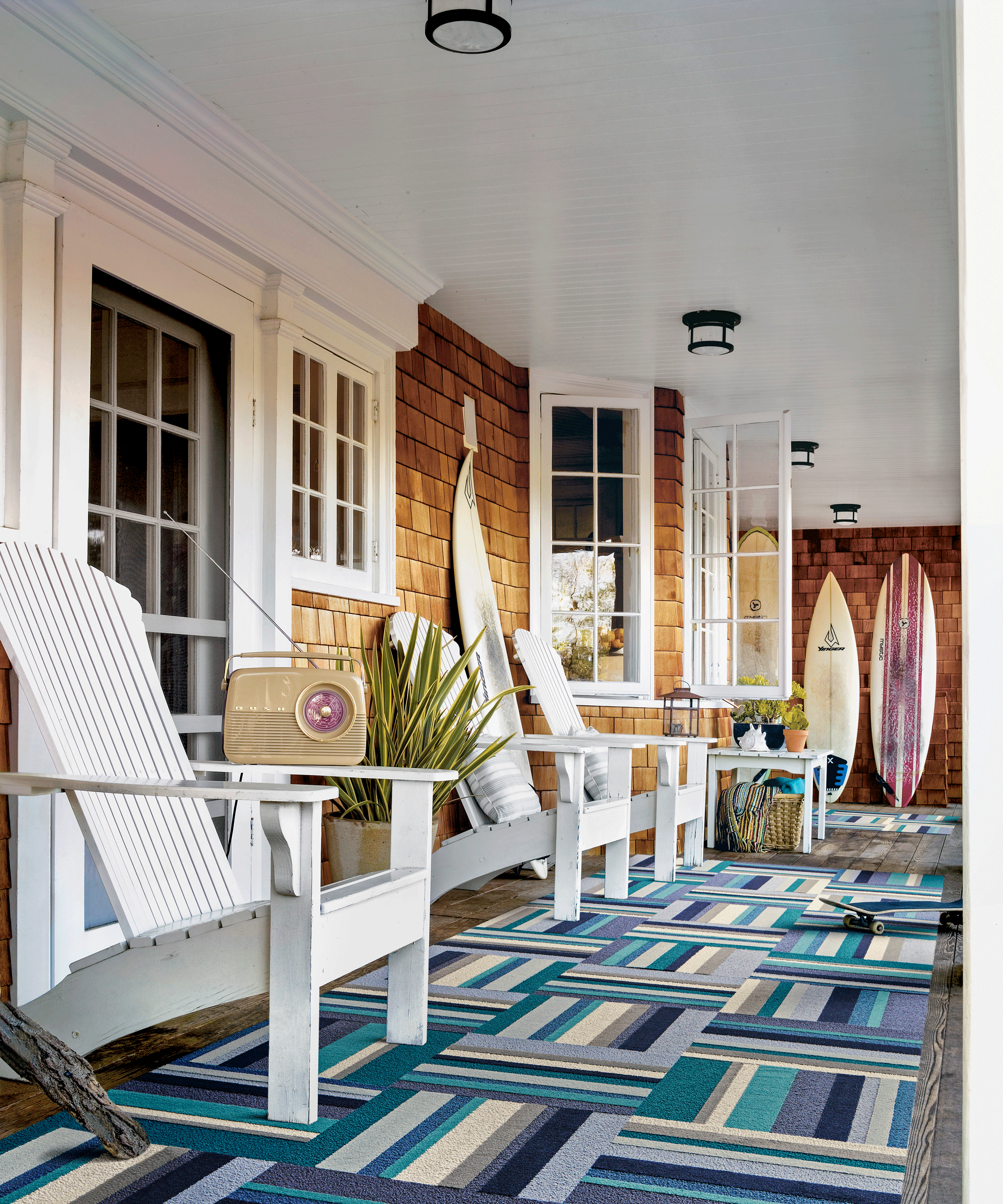 Surf inspired porch with wooden deck chairs, blue patterned rug, and surf boards.