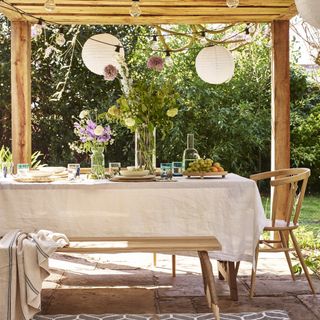 Table under a canopy in a garden accessorised with table cloth and flowers.