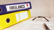 Yellow and purple binders with freelance label sitting next to a pair of glasses