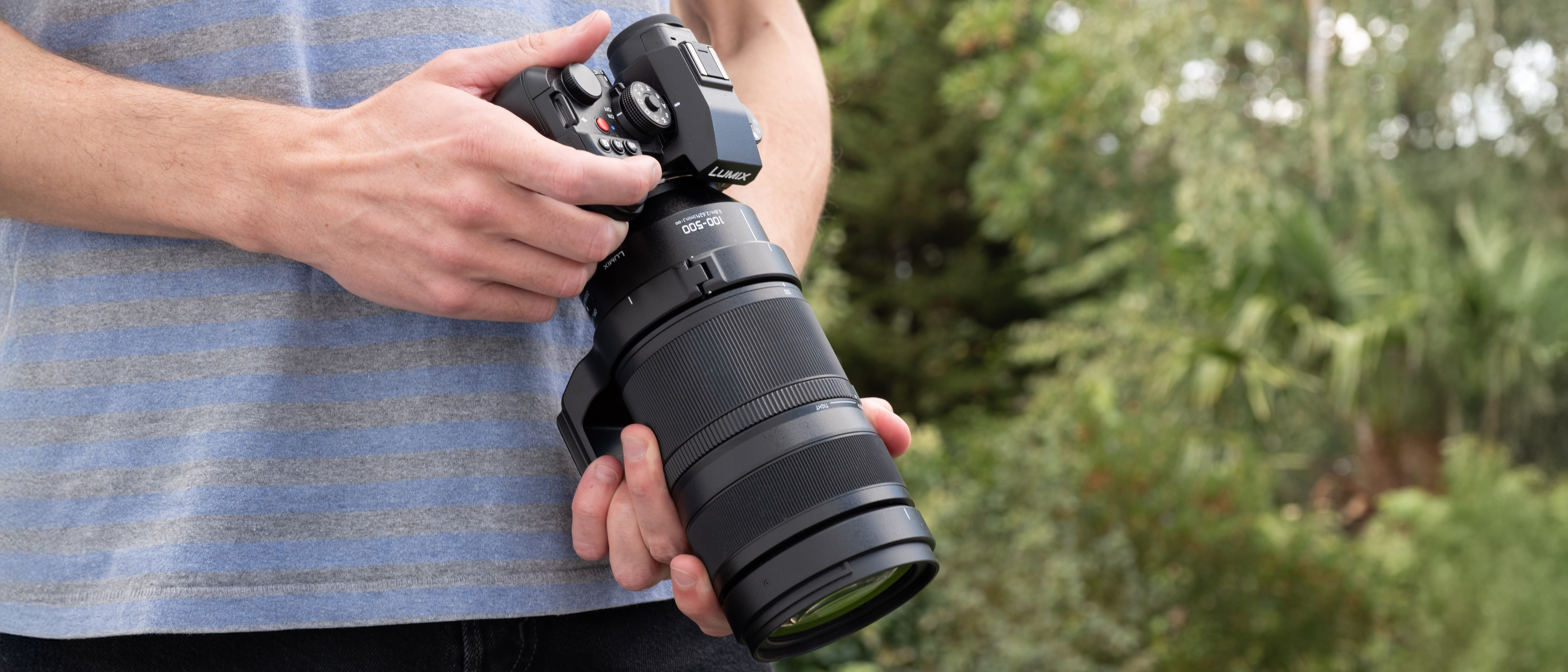 Panasonic Lumix S1II camera with a Lumix S 100-500mm f/5-7.1 lens attached held in a pair of hands outdoors
