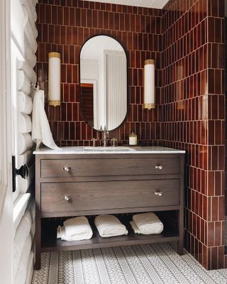 A bathroom with tiles in ox blood red with a wooden cabinet