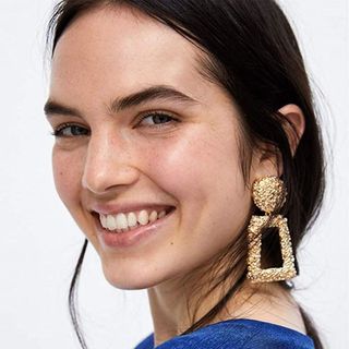 A close up of a person smiling with gold dangling earrings