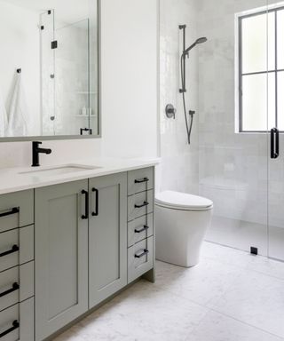 white tiled bathroom with a gray-green built in furniture unit and a matt black shower