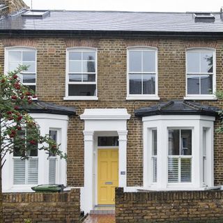 house exterior with bricked wall and white window and yellow door