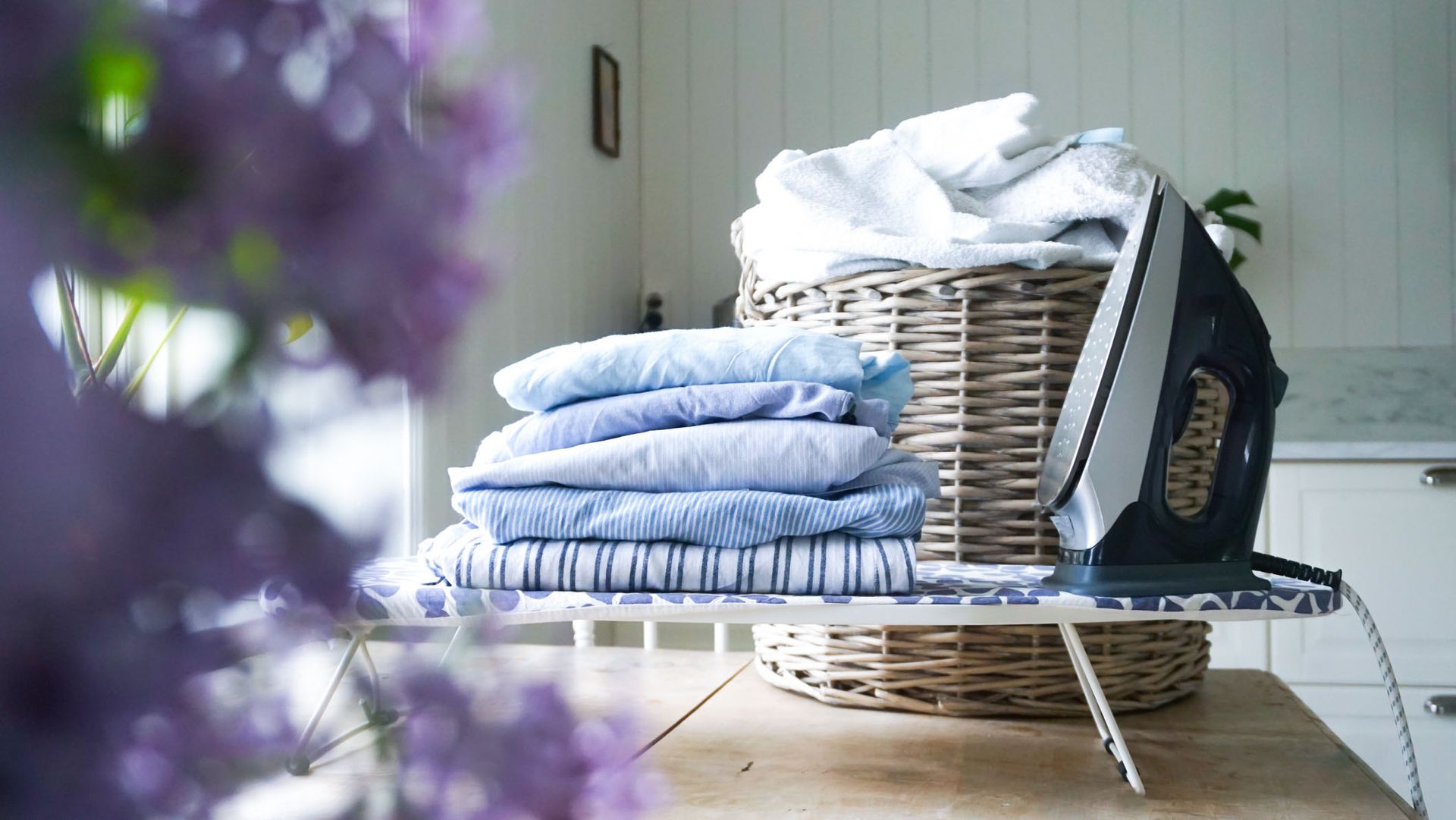 An iron on an ironing board with clean clothes piled next to it