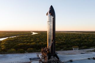 a black bellied chrome spaceship stands on a concrete pad with a winding creek in the distance.