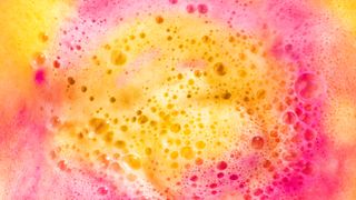 Pink and yellow bath bomb dissolving in the water. - stock photo