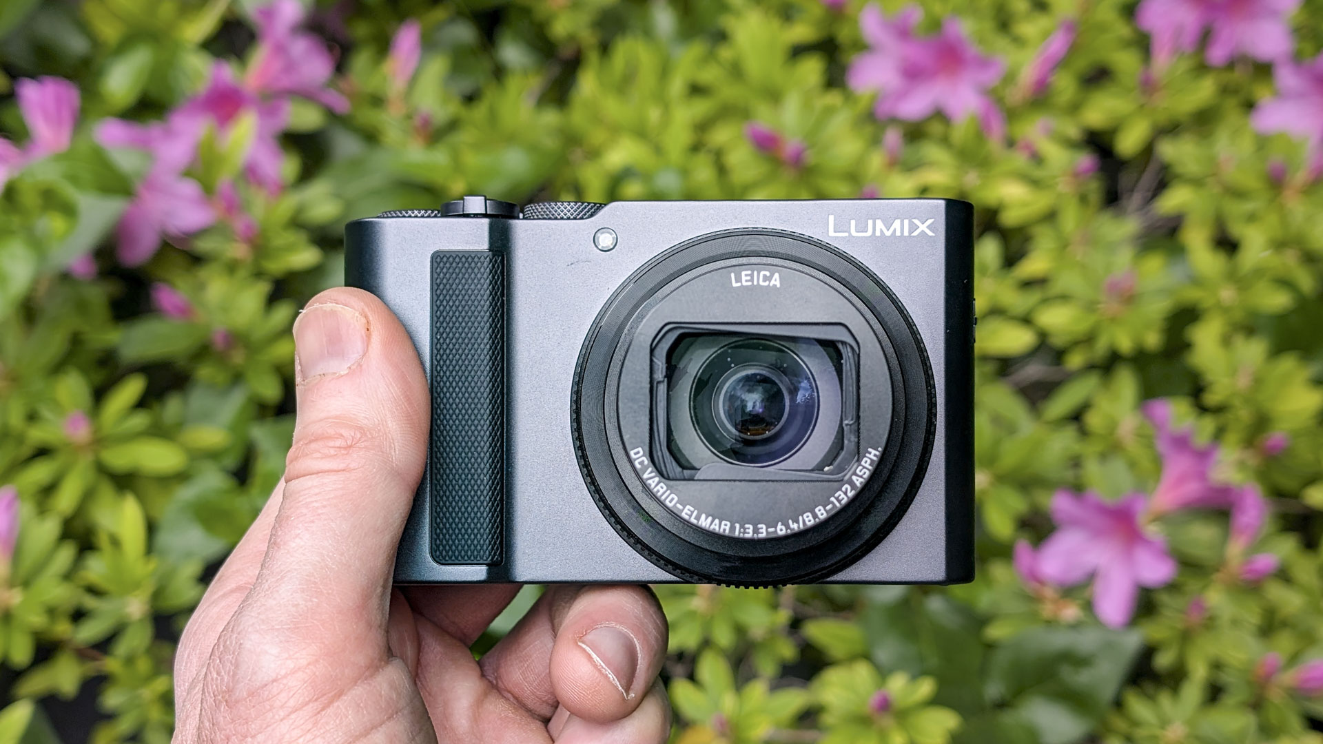 Panasonic Lumix TZ300 compact camera in the hand with a colorful floral backdrop