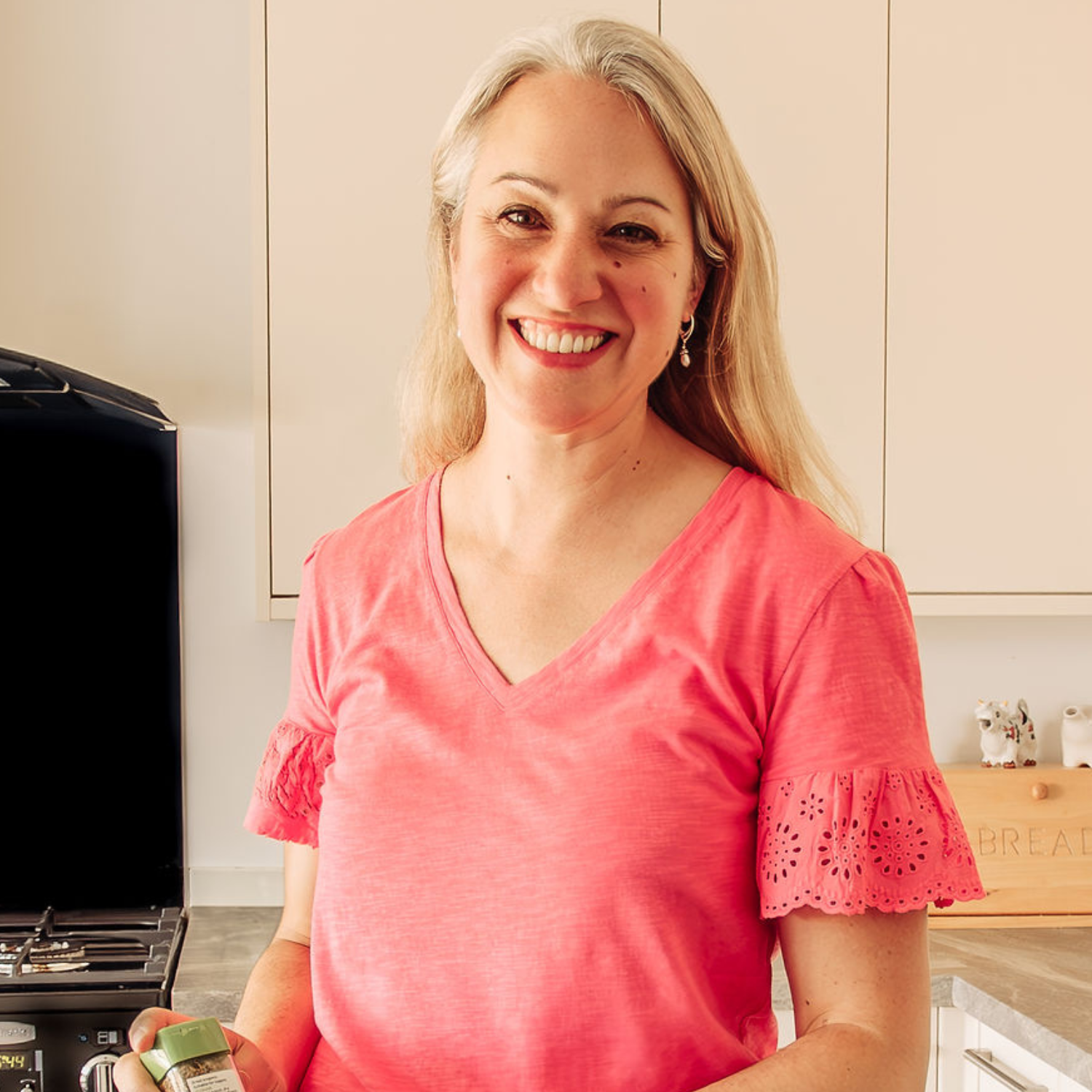 A woman in an orange v-neck with lace hemmed sleeves in a kitchen