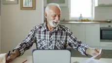 An older man appears happy as he looks over financial paperwork at his kitchen table.
