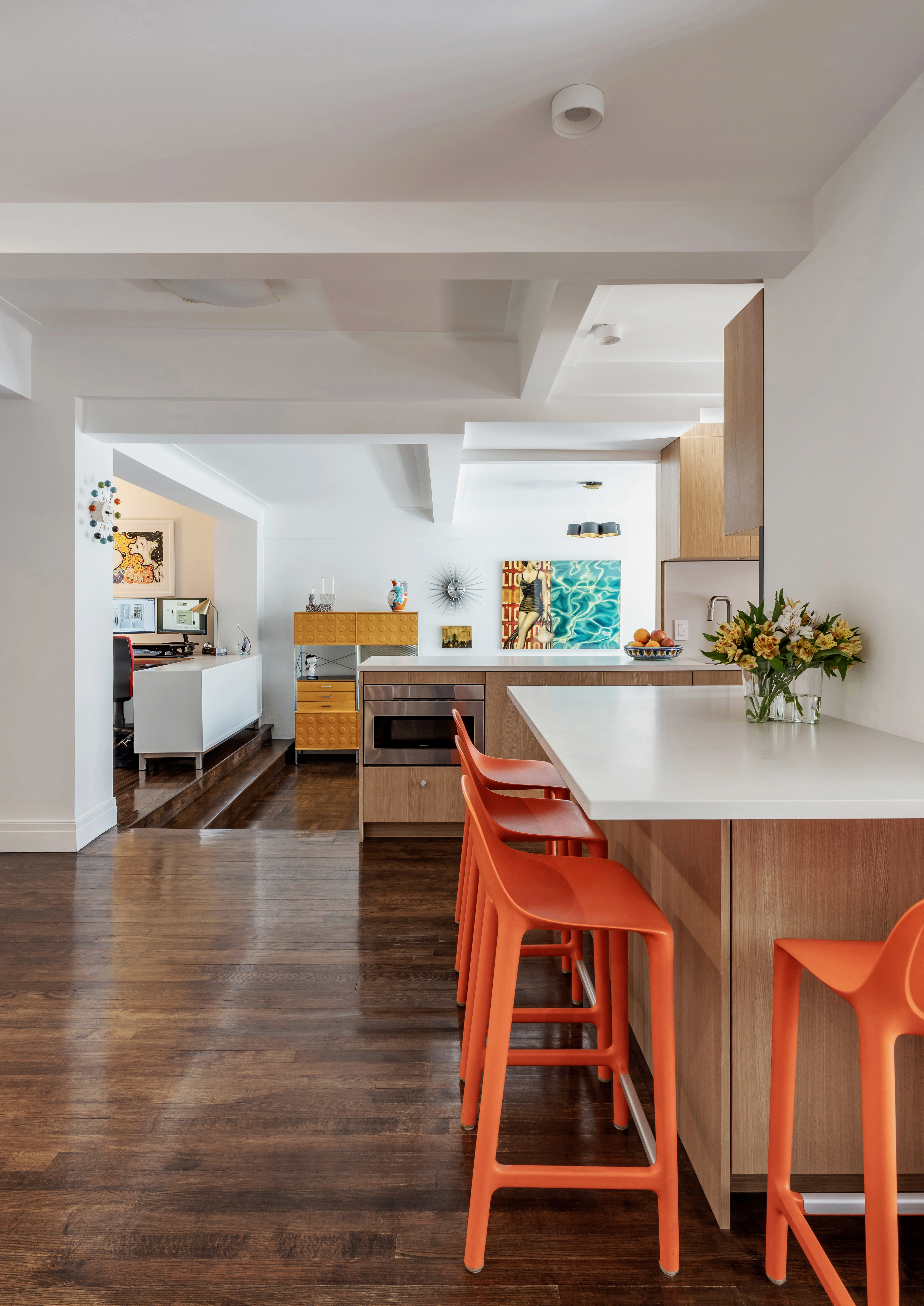 A galley kitchen with wooden cabinets, and a countertop with orange bar chairs