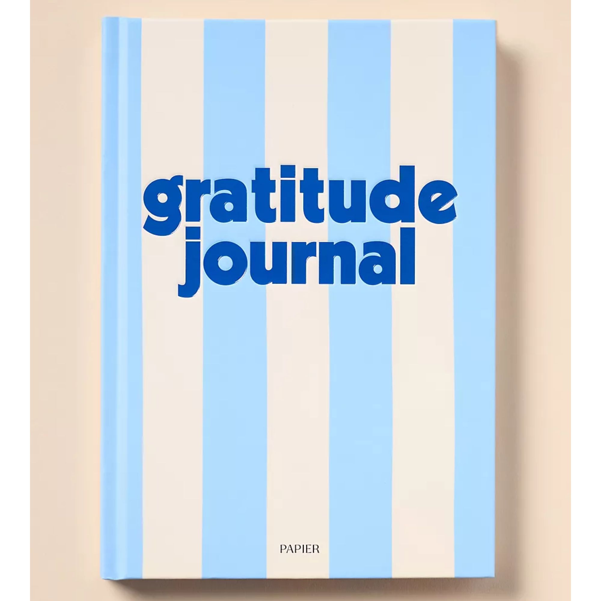 A blue and white stripped journal with the words 'gratitude journal' printed on the front in large, bold, blue letters. 