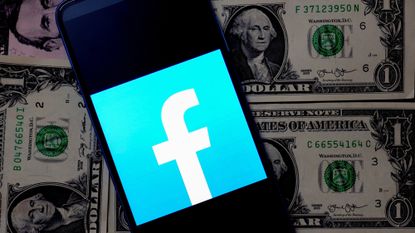 The Facebook logo, displayed on a smartphone, on top of a stack of American dollar bills